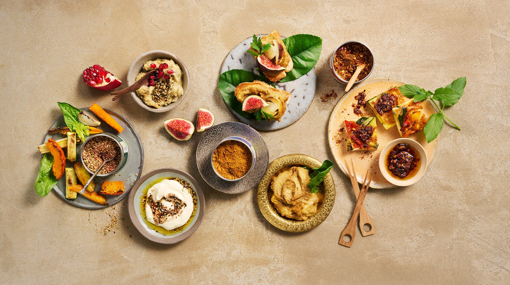 Orientalische Gewürze Harissa, Ras el Hanout und Za'atar mit Dips und Gemüse auf rustikalem Tisch